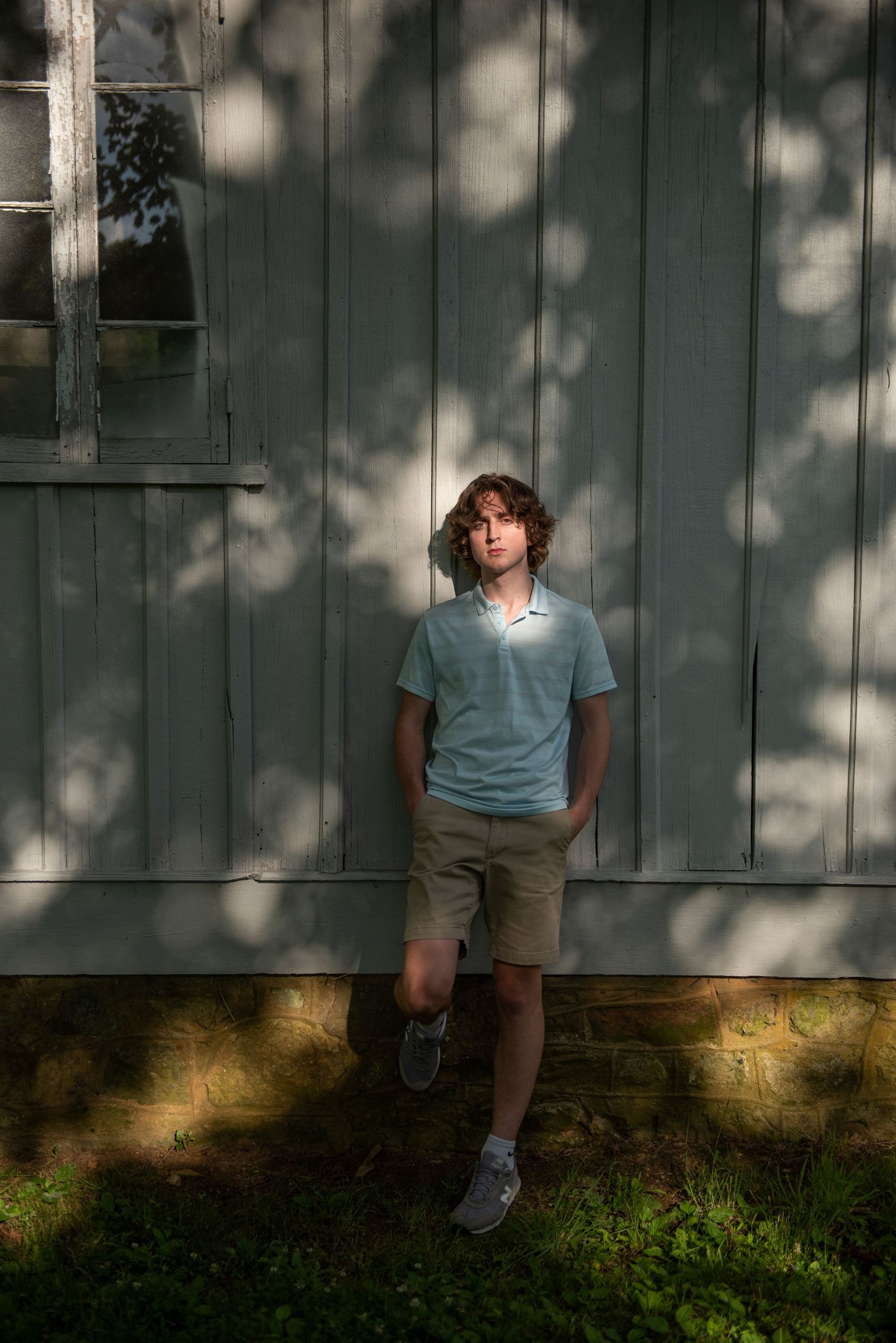 Casual portrait against weathered green barn wall with dappled sunlight.