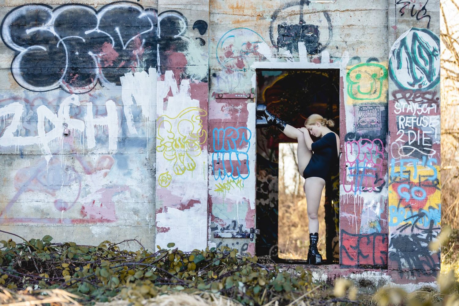 A figure wearing white stands in a doorway surrounded by colorful graffiti and urban street art on concrete walls.