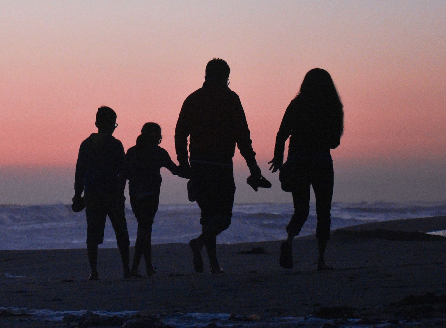 Silhouette of family walking on beach at sunset holding hands.