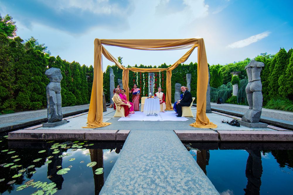 Beautiful outdoor wedding ceremony setup with gold canopy and reflecting pools under blue sky at garden venue.