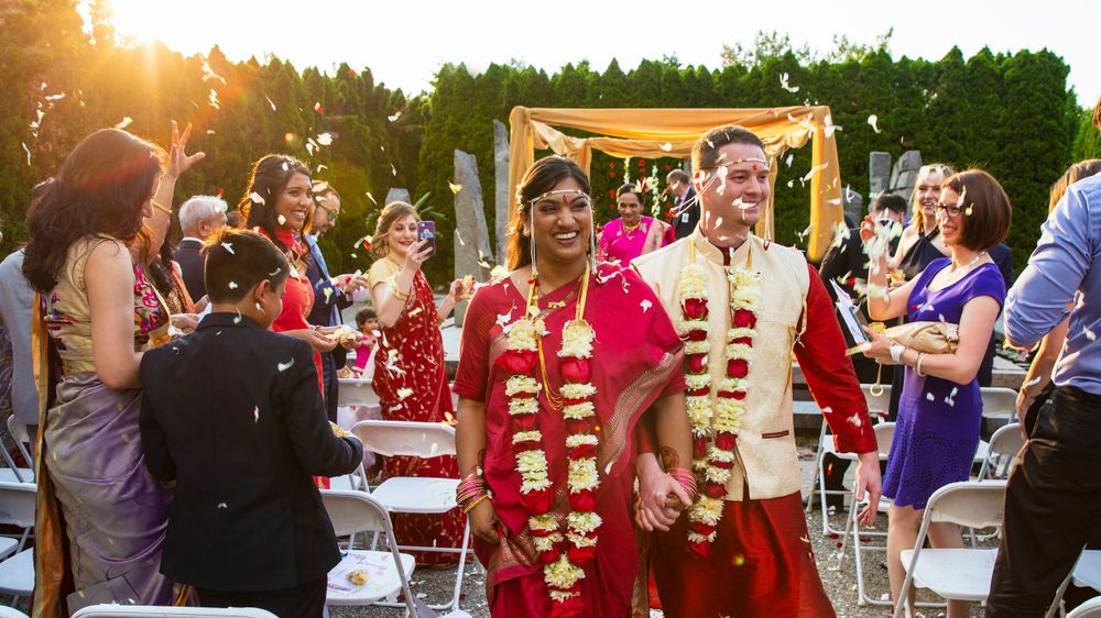 An outdoor wedding ceremony during golden hour where a couple stands together wearing traditional Indian and western attire.