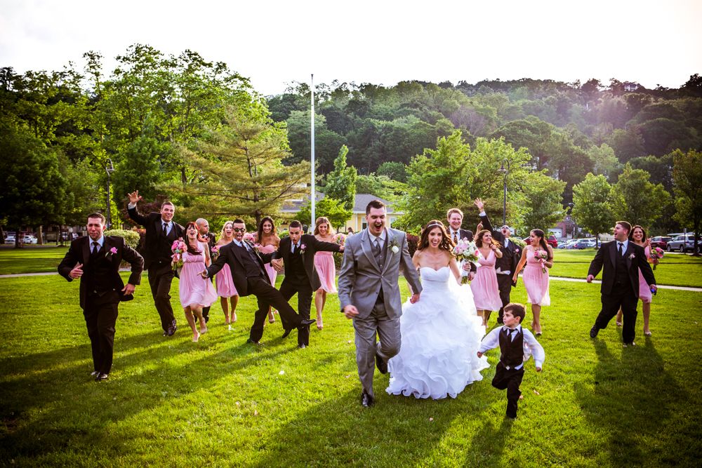 Wedding party runs and celebrates on a grassy hill during sunset at an outdoor reception.