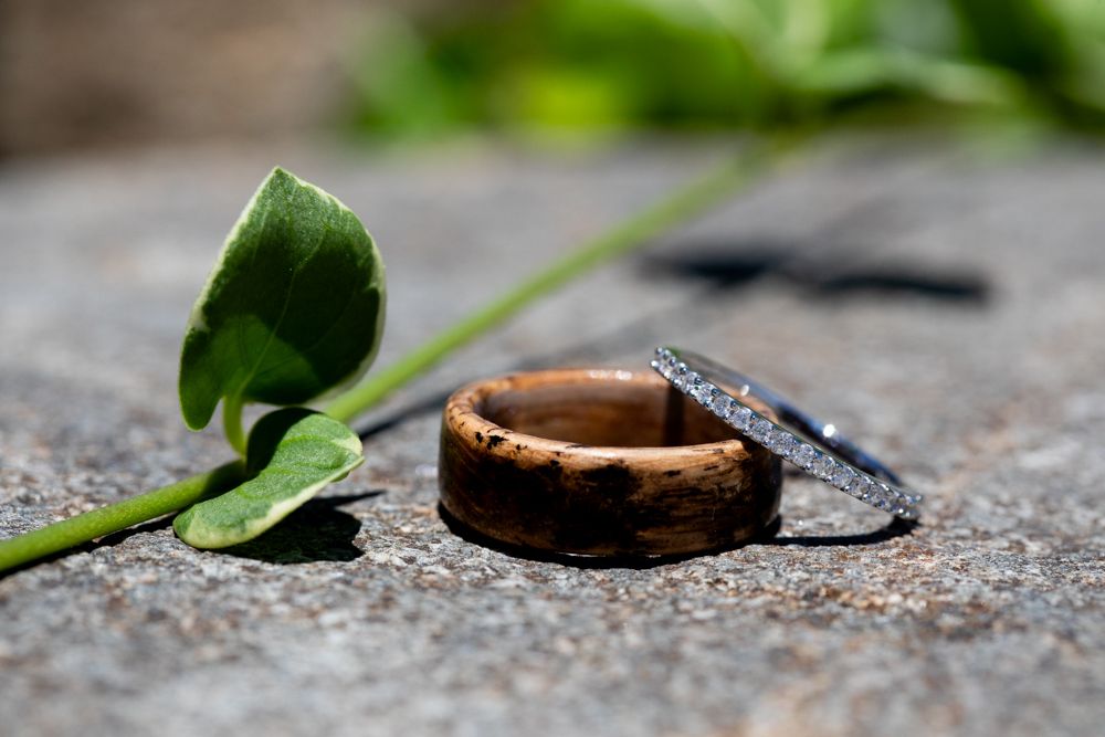 Wedding rings displayed on stone surface with green leaf accent.