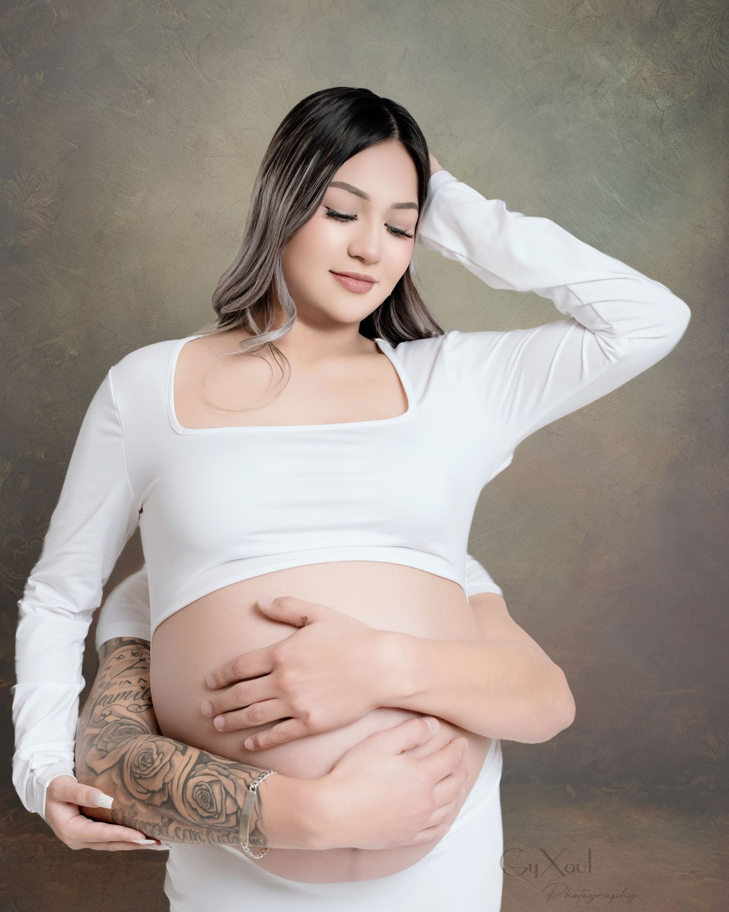 Intimate maternity photo with woman in white crop top showing tattoos.