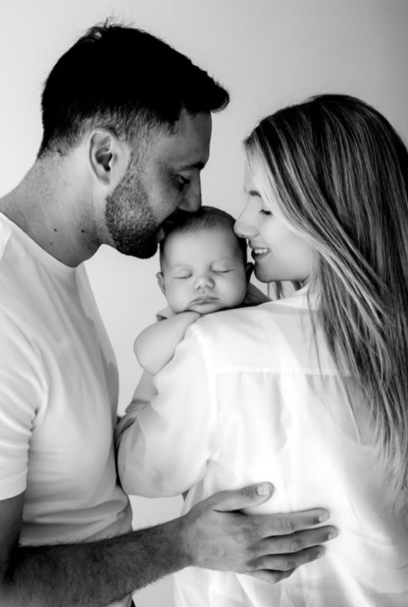 Black and white photo of parents tenderly kissing their sleeping newborn baby.