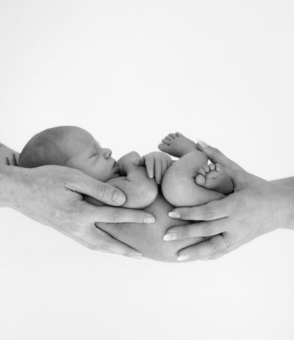 Black and white newborn baby cradled gently in parents hands.