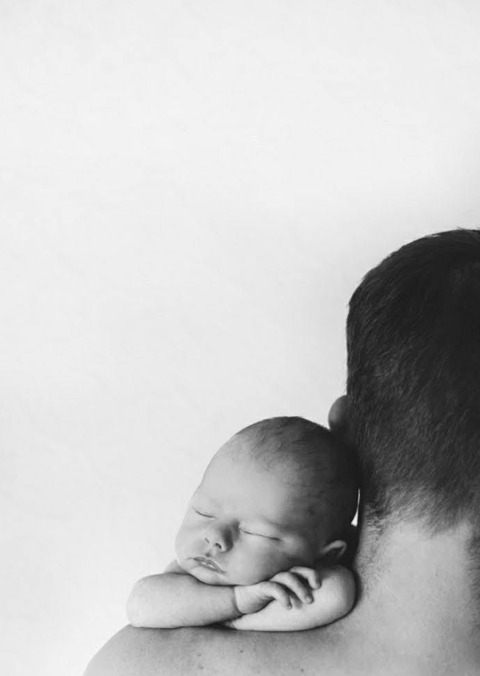Black and white photo of sleeping newborn resting on fathers shoulder.
