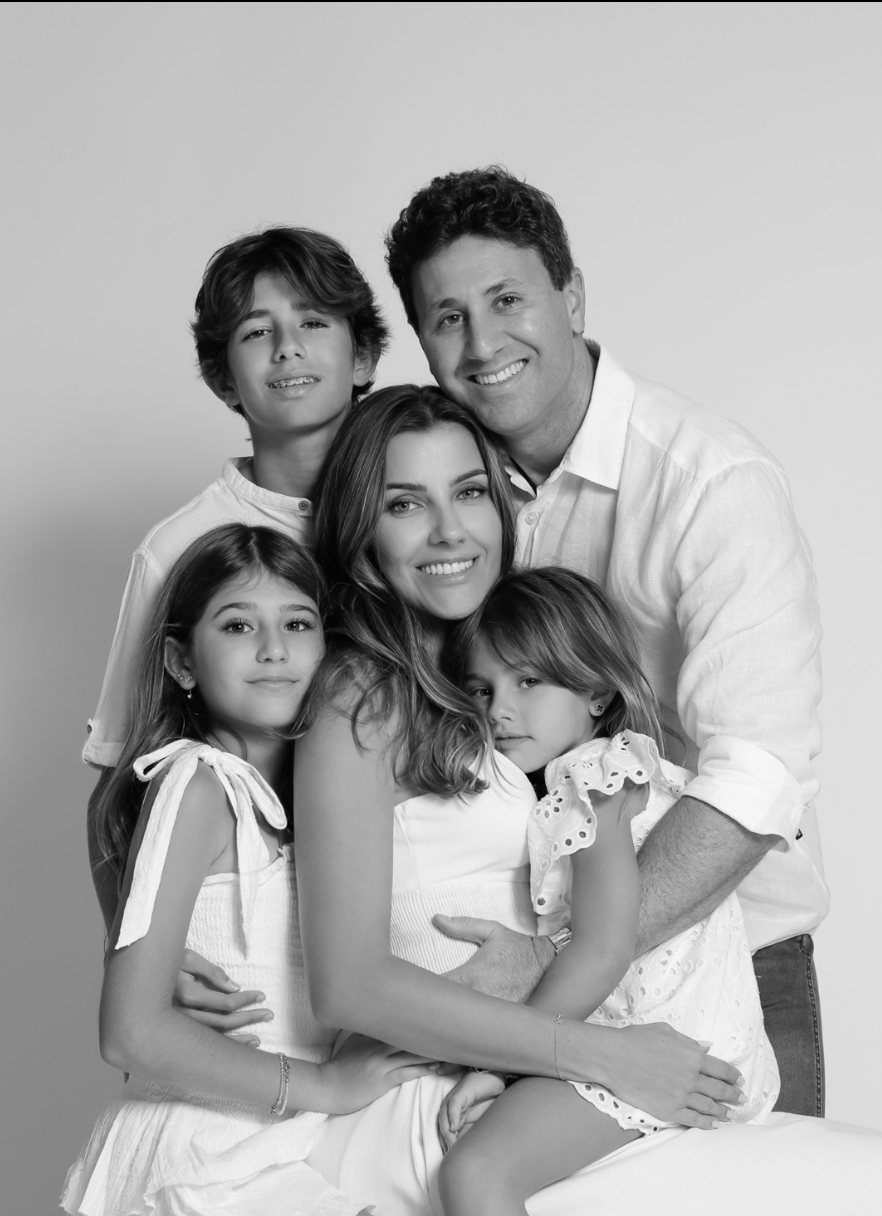Black and white family portrait of parents with three children smiling together in matching white outfits.