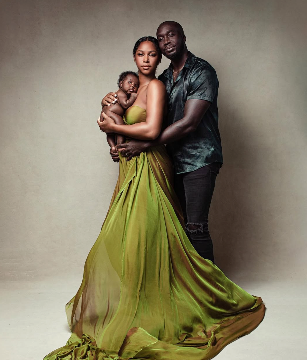 Elegant family portrait of a couple in formal attire holding their newborn baby, woman in flowing green gown.