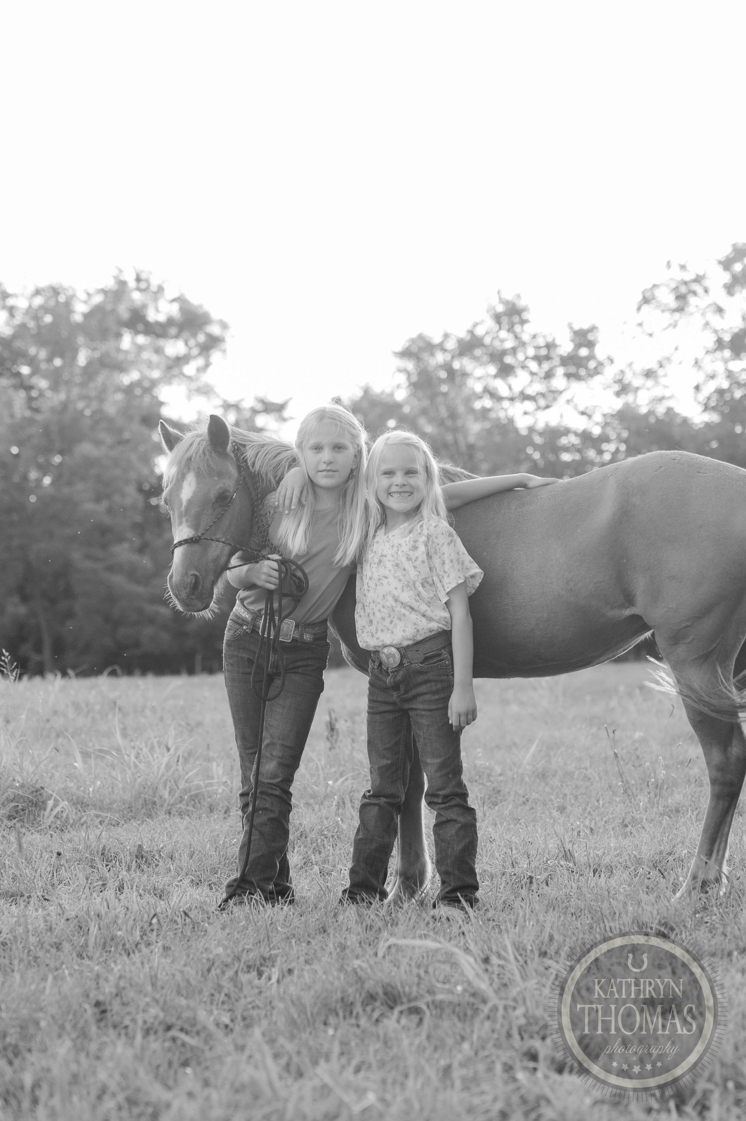 Two youth stand with a brown horse in a rural field setting.