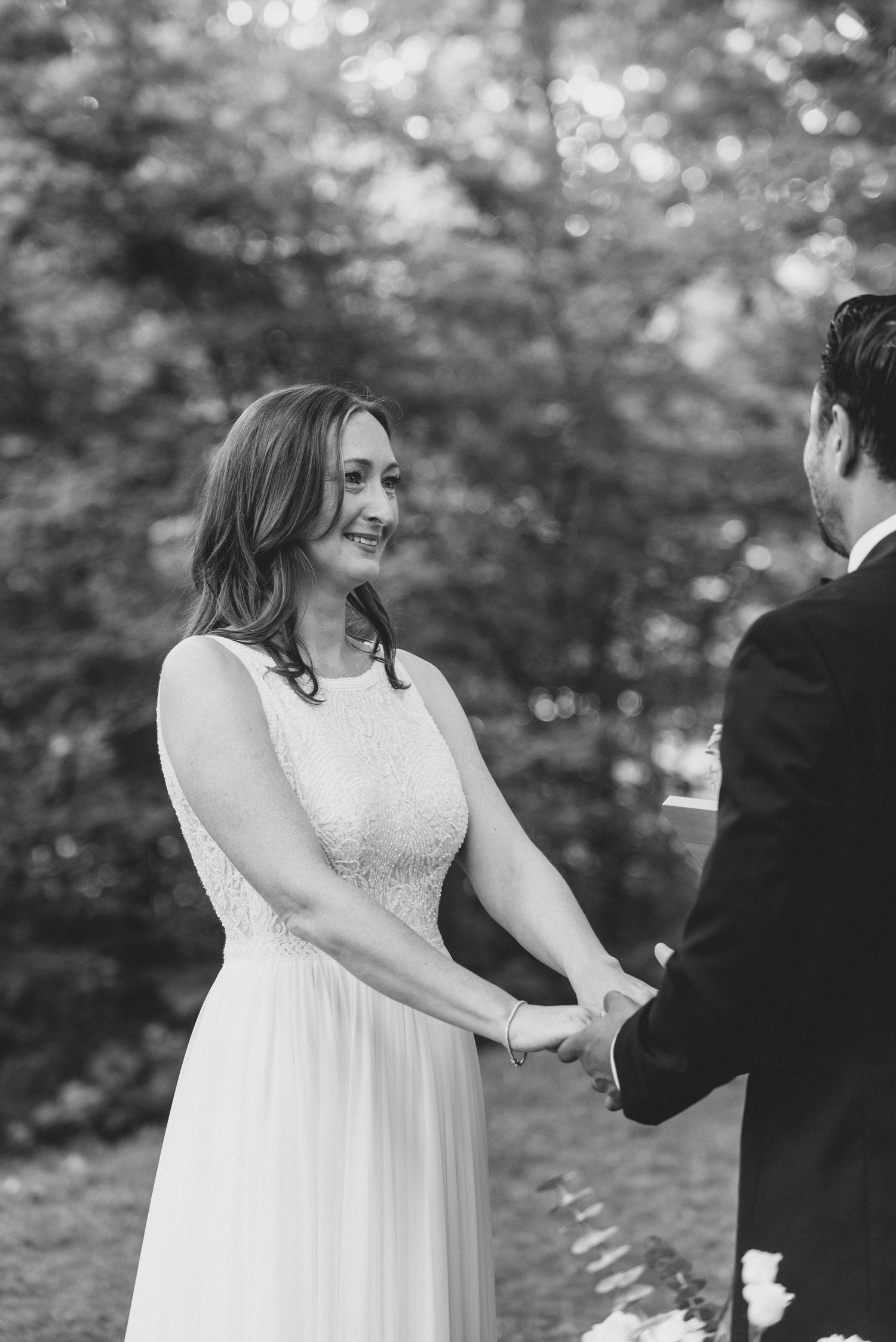 A couple holds hands during a black and white wedding ceremony in a romantic outdoor garden setting.