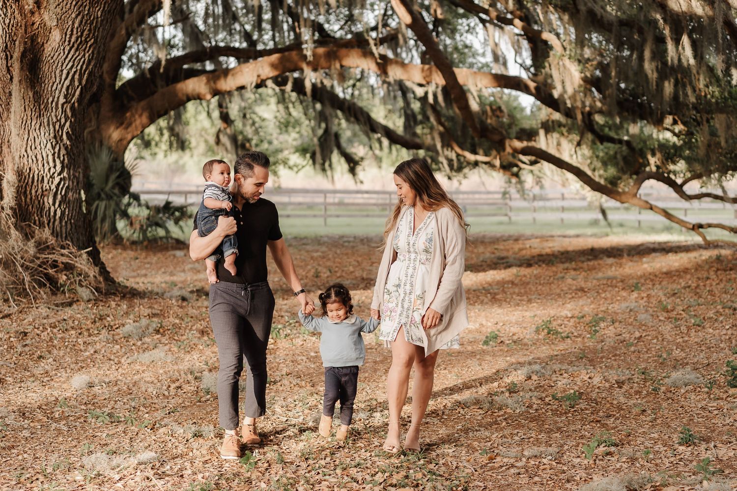 A family of three posing together outdoors in a park setting during golden hour.