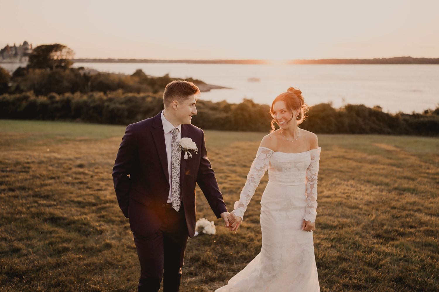 A couple walks along a coastal field during golden hour sunset.