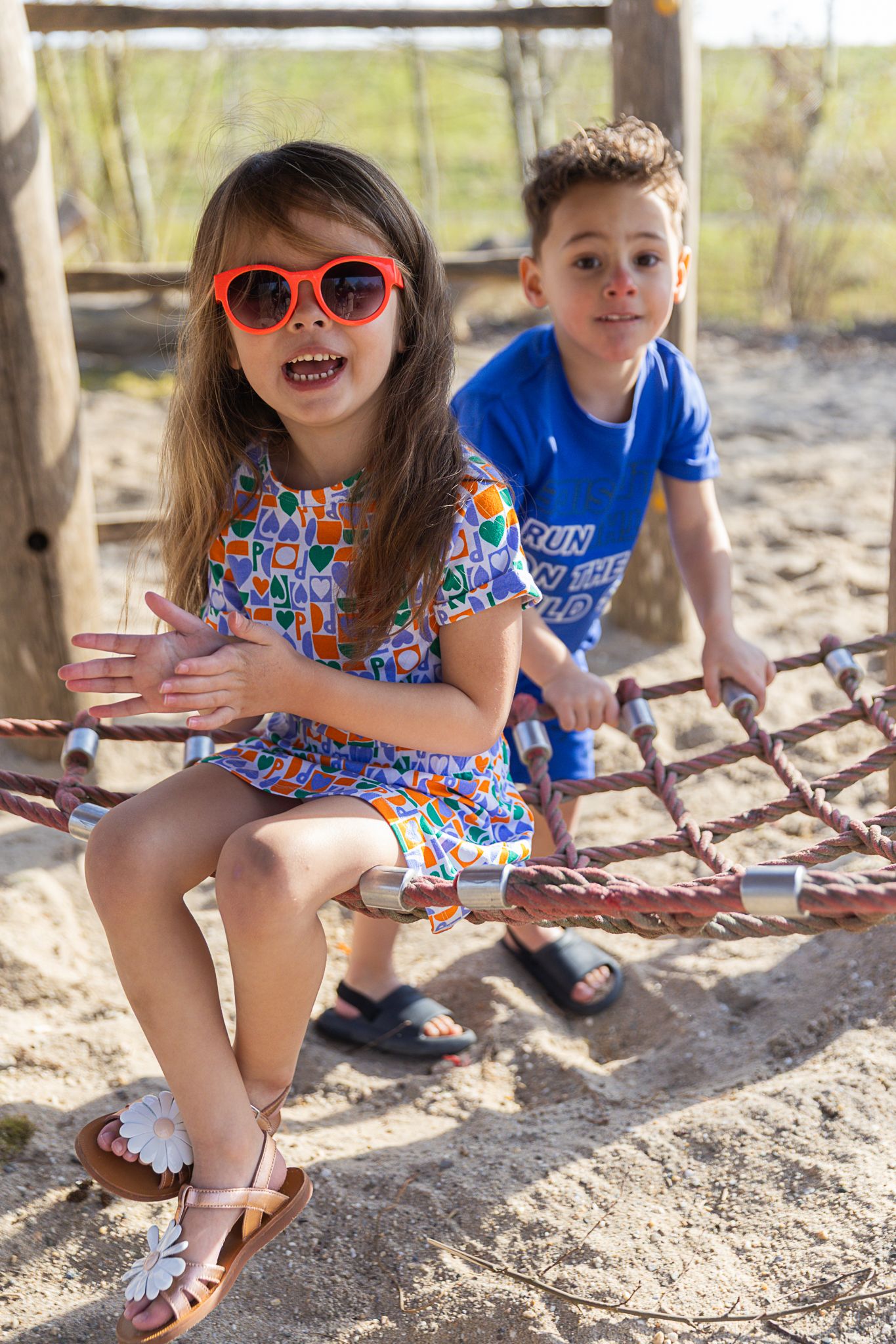 Two children sitting on playground equipment on a sunny day. Campagne shoot kinderkleding.