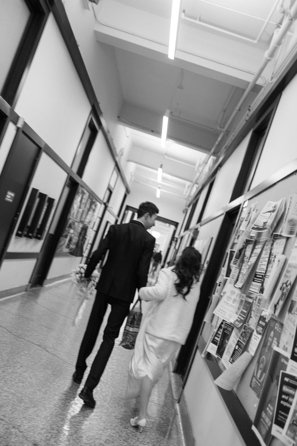 A couple walking down a corridor in formal attire, shot in black and white.