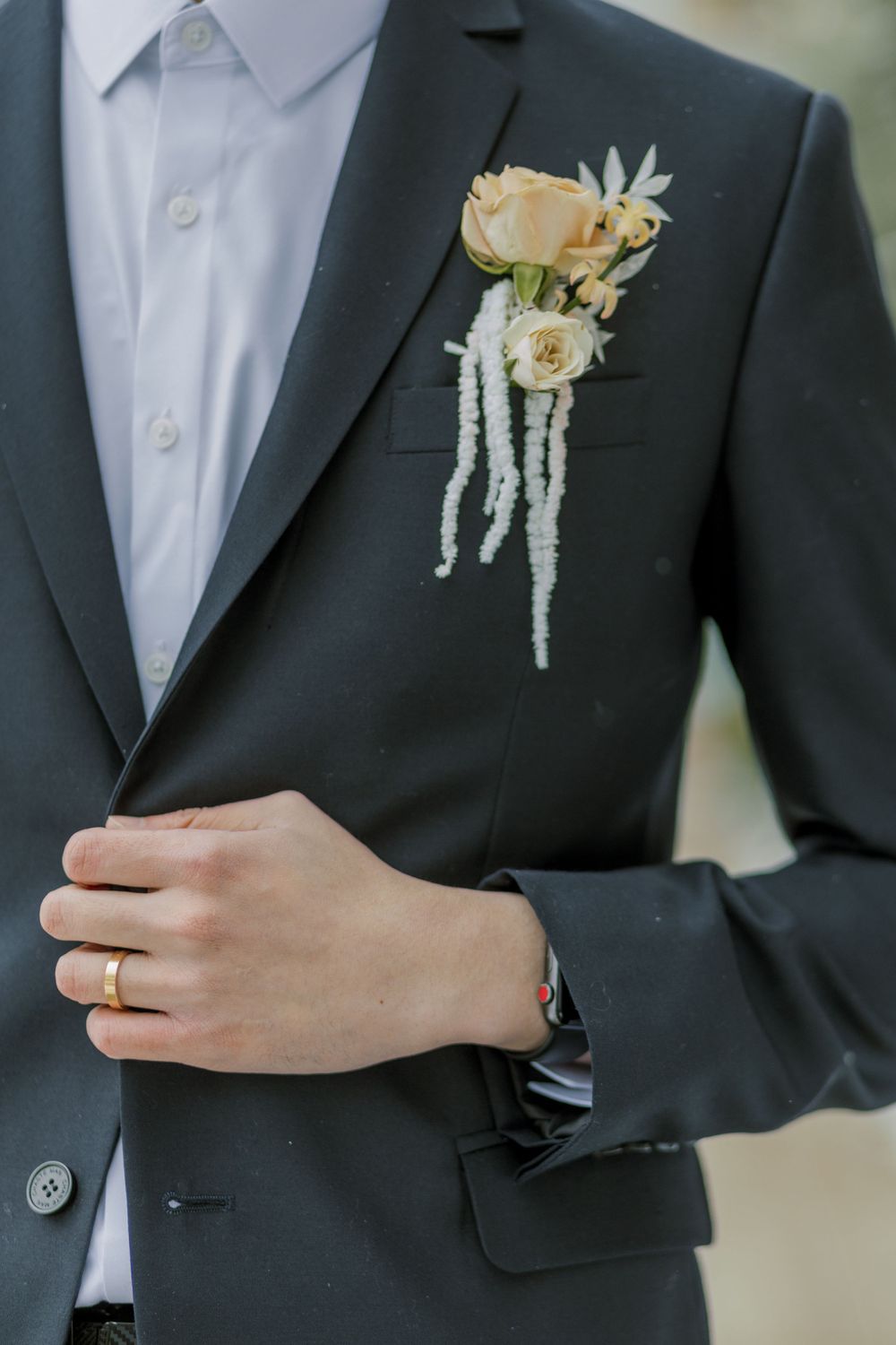 A cream and white boutonniere pinned to a dark suit jacket.