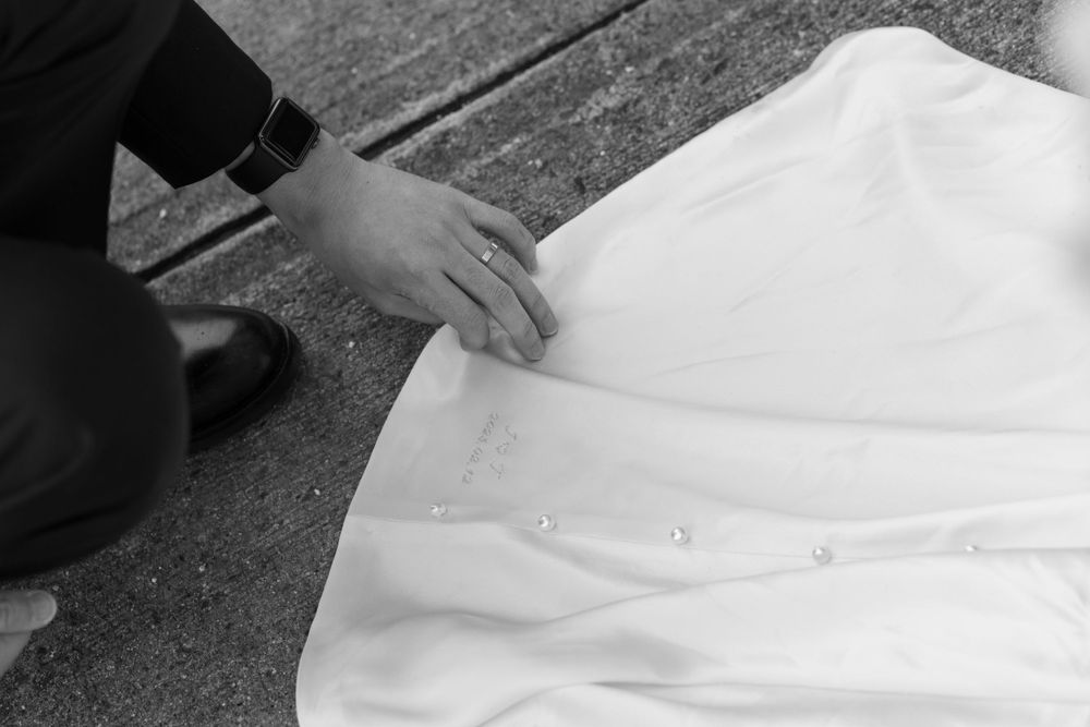 Black and white photo of hands adjusting a white wedding dress hem.