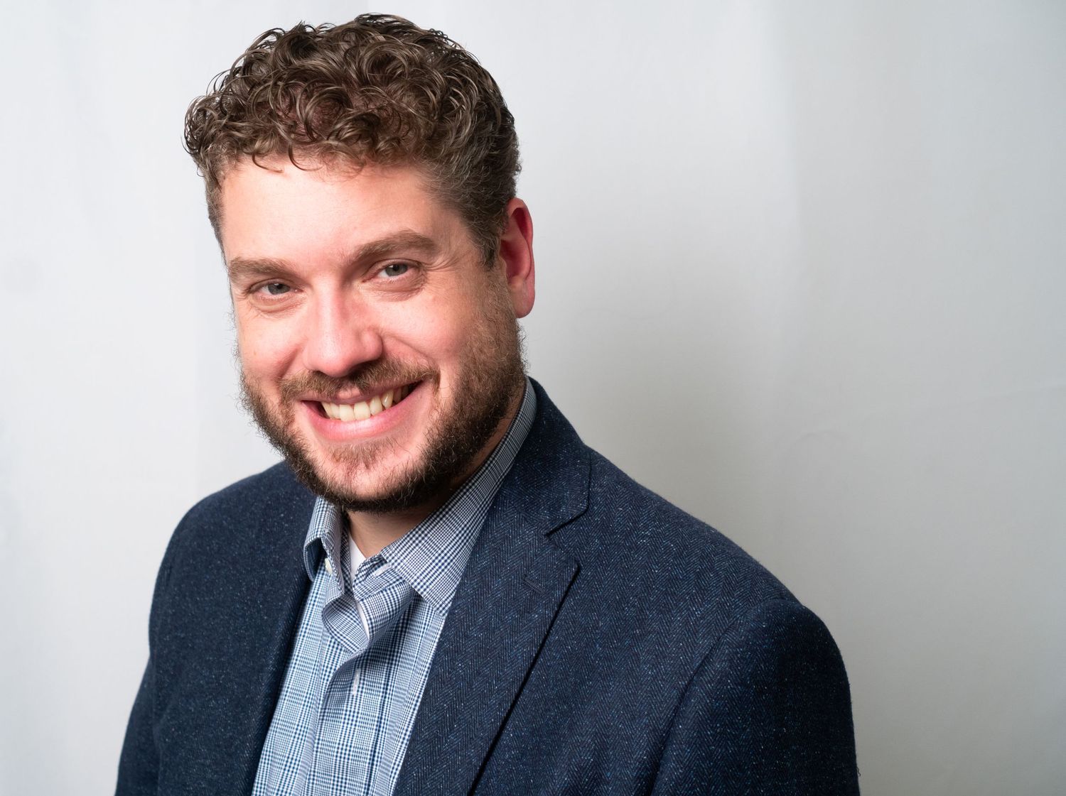 Professional headshot showing warm smile wearing navy suit jacket against a white backdrop.
