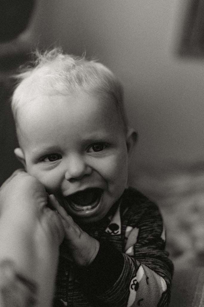 Black and white close-up of a giggling baby being held, showing a big toothy smile with pure joy.