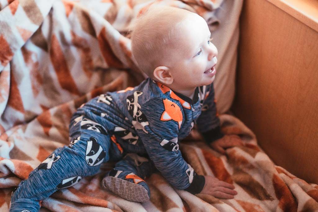 Baby in fox-print pajamas playing on a brown blanket.