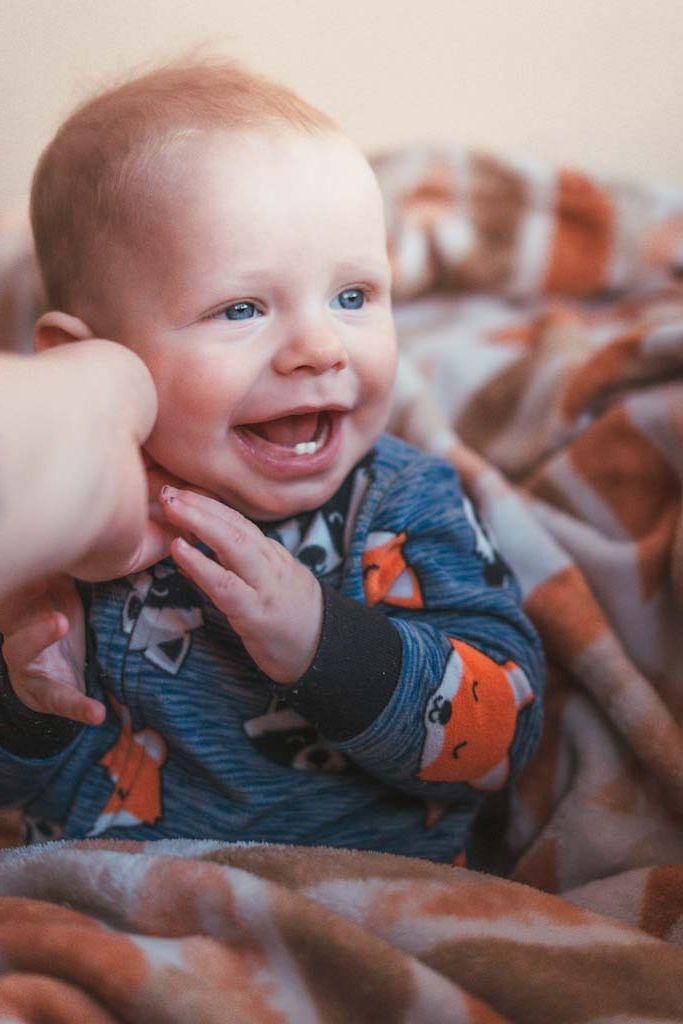 Smiling blue-eyed baby in fox pajamas laughing on a cozy blanket.