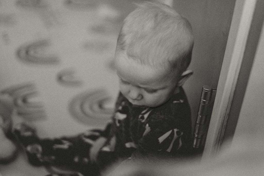 Black and white close-up of a baby sitting by a door on patterned floor.