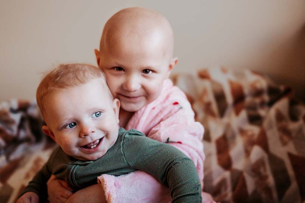 Two young children smiling and hugging on a patterned blanket.