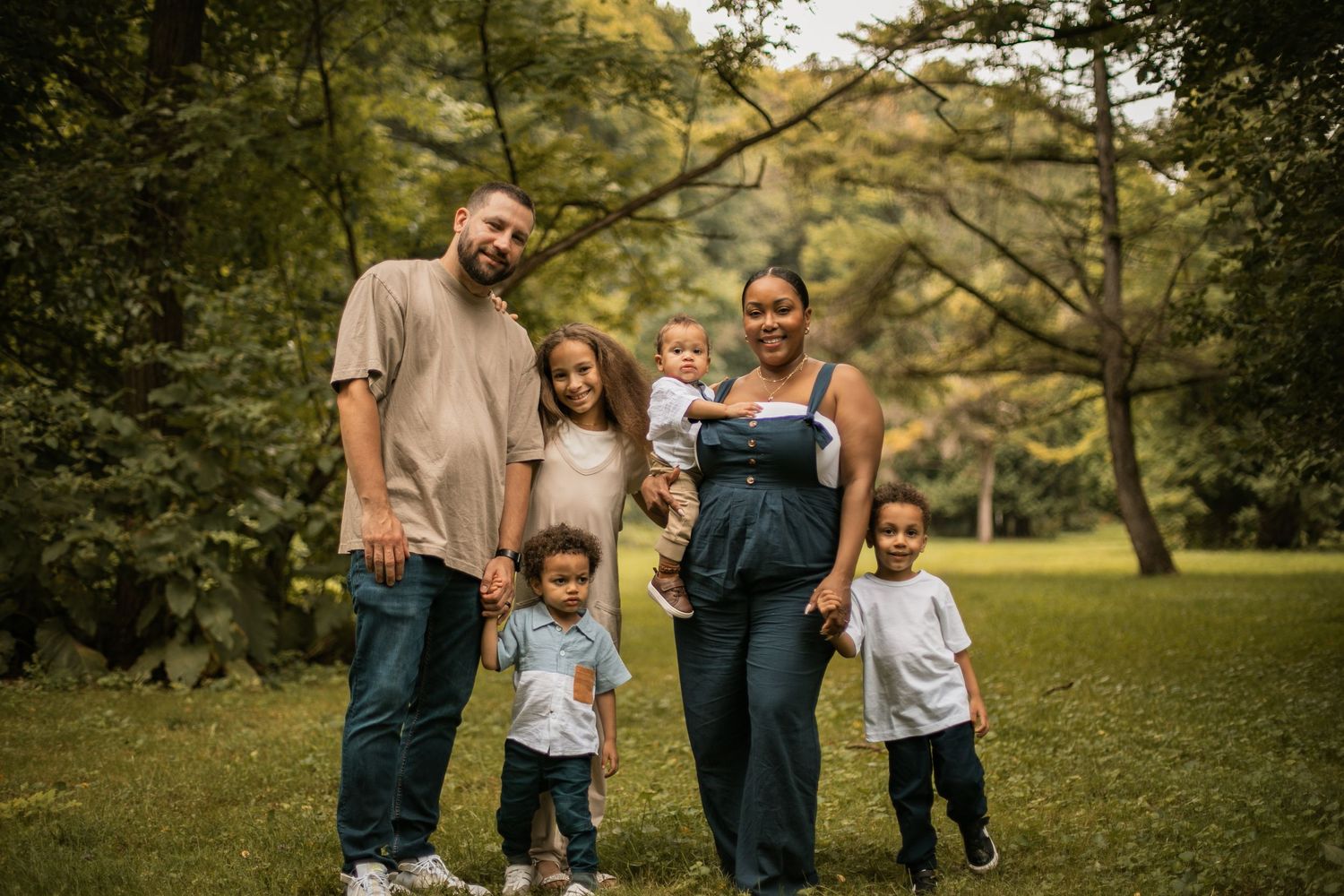 A family poses together against a rustic stone wall backdrop surrounded by lush greenery in a warm outdoor setting.