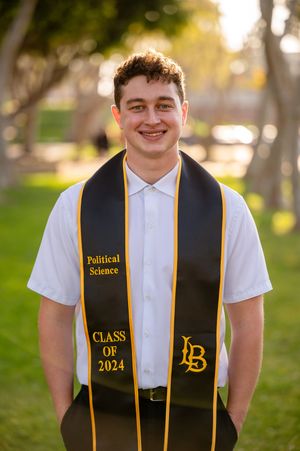 Graduate in white shirt wearing black and gold Political Science graduation stole for Class of 2024 on sunny campus lawn.