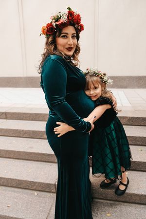 Maternity moment on stone steps with matching teal velvet dresses and floral crowns.