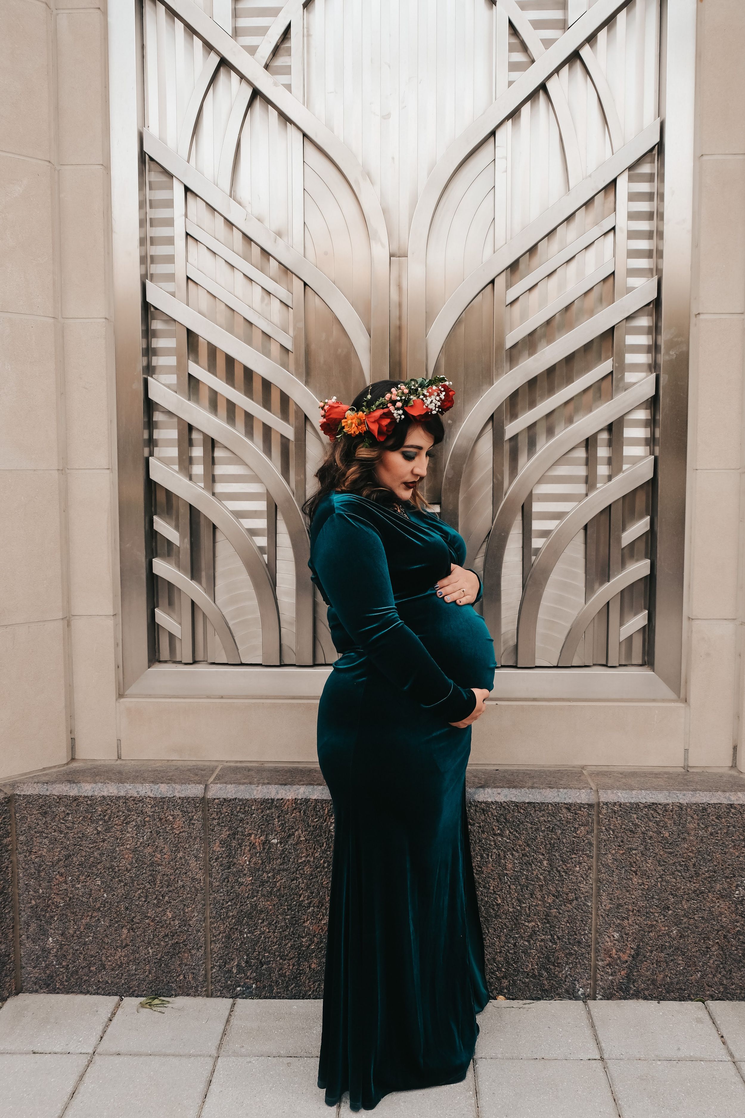 Maternity portrait in teal velvet dress against geometric Art Deco wall design.
