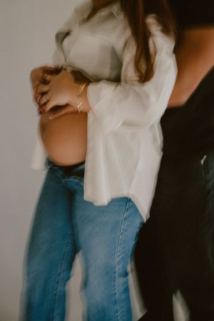 A couple embraces while wearing a white shirt and blue jeans in a moody indoor photoshoot.