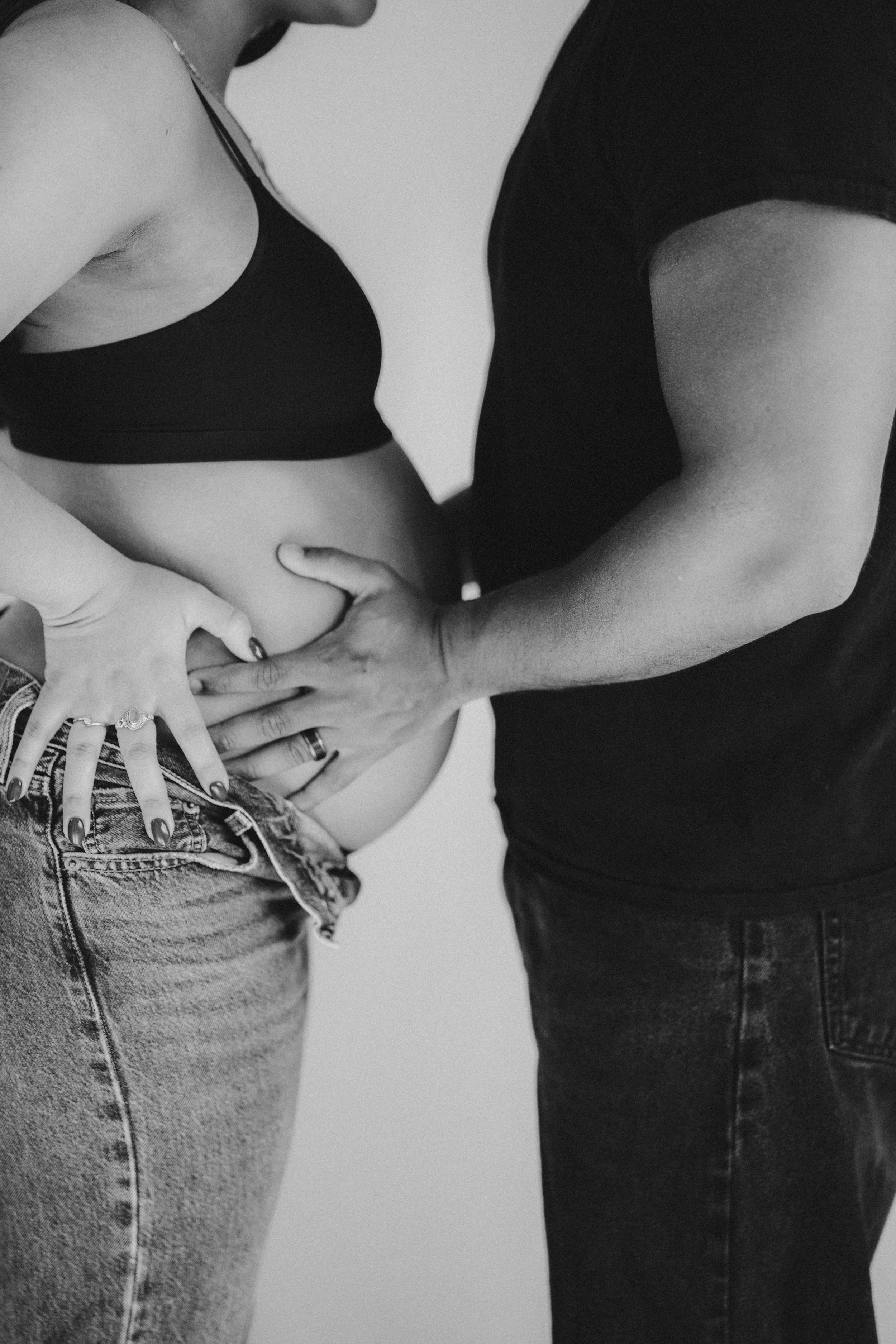 Black and white intimate photograph showing hands resting on denim-clad hip.