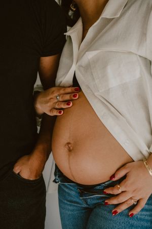 Close-up maternity photo showing red nails and white button-down shirt.