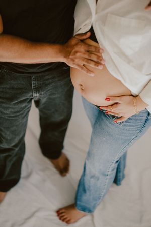 Intimate maternity portrait with gentle hands on belly against white background.