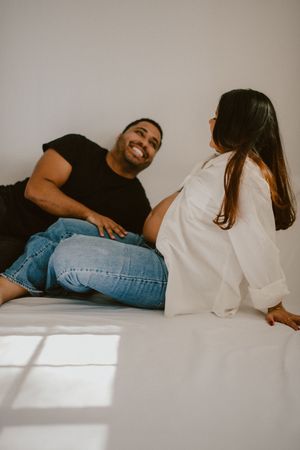 A couple shares a joyful moment together while sitting on a white surface in casual attire.