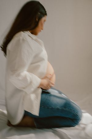Side profile of an expectant mother in white shirt and jeans against a light backdrop.