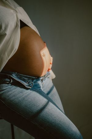 An artistic side view of a pregnant belly with sunlight creating dramatic shadows.