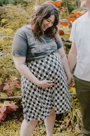 Maternity photo in a garden with vibrant fall foliage and a checkered pattern dress.