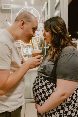 Maternity photo in front of neon signage sharing a milkshake together.
