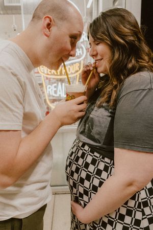 Candid maternity moment sharing drinks in front of illuminated storefront.