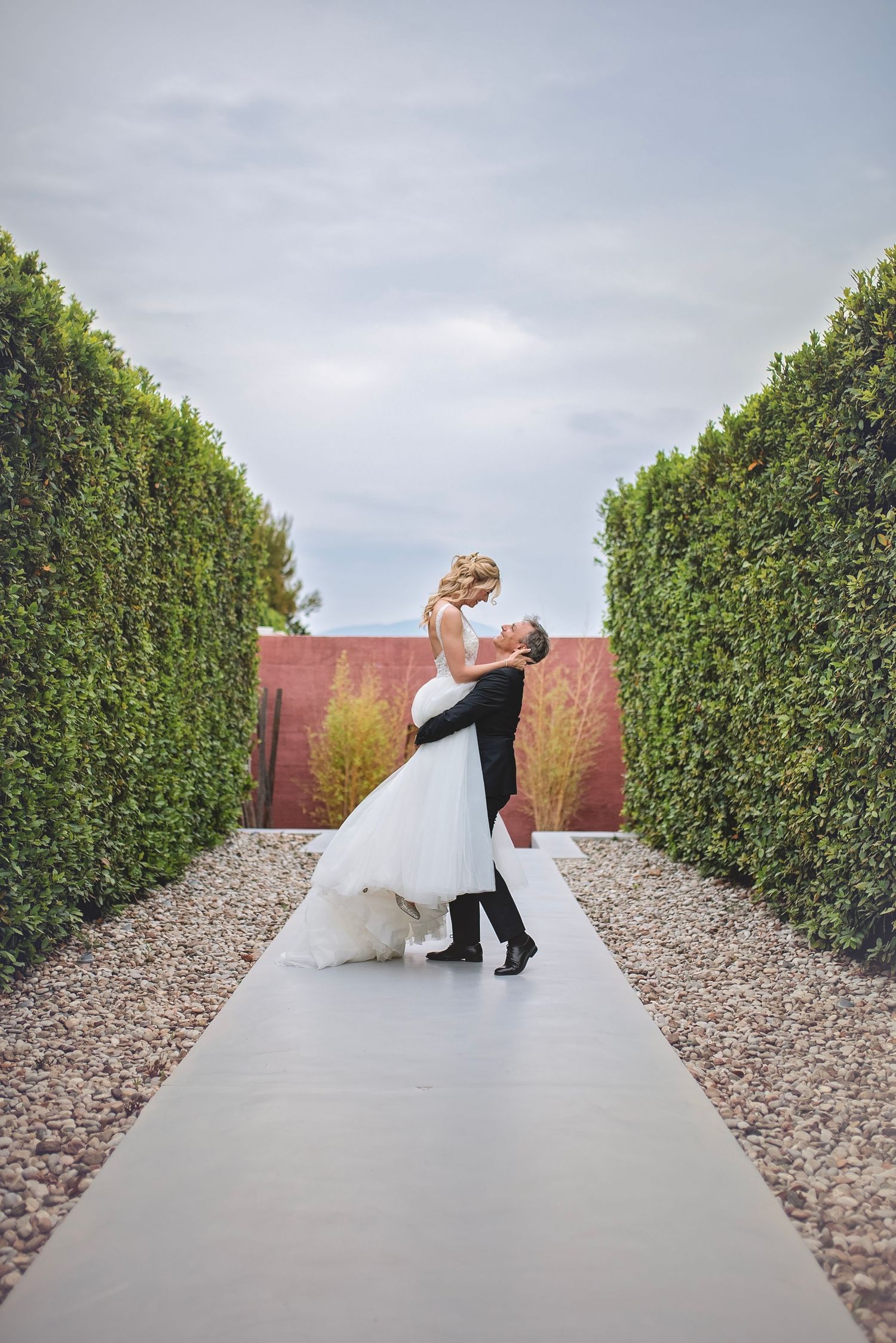 A romantic wedding dip pose between hedges on a modern garden pathway.
