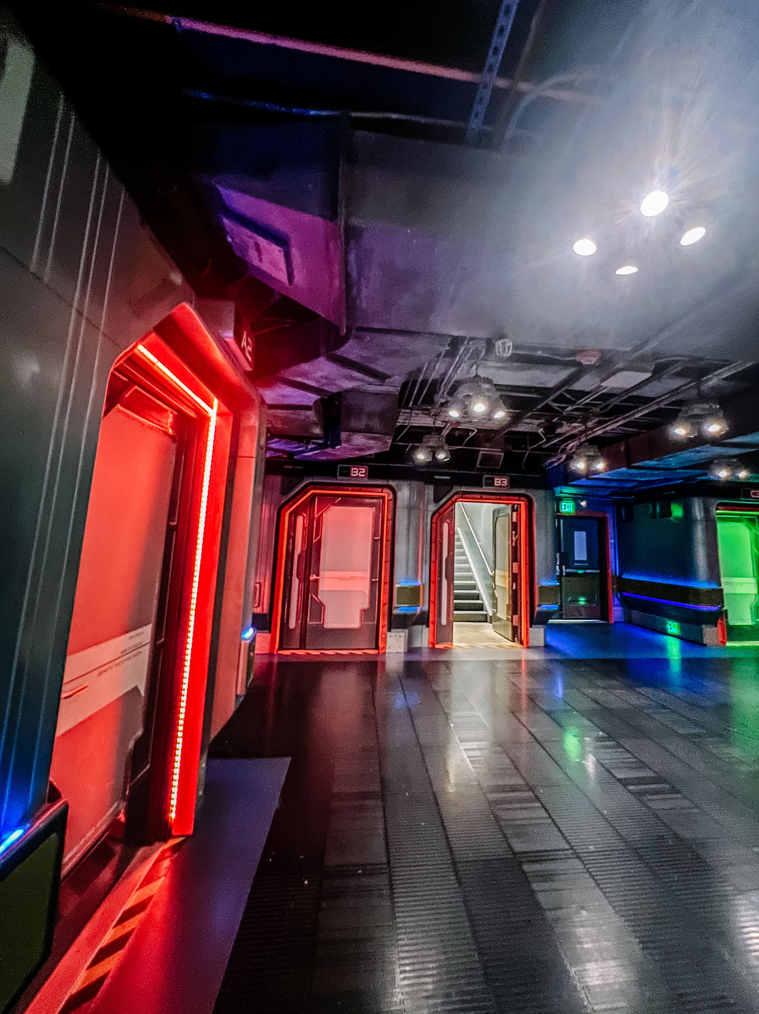 Modern nightclub interior hallway with dramatic red, blue and green LED lighting and industrial-style ceiling design.