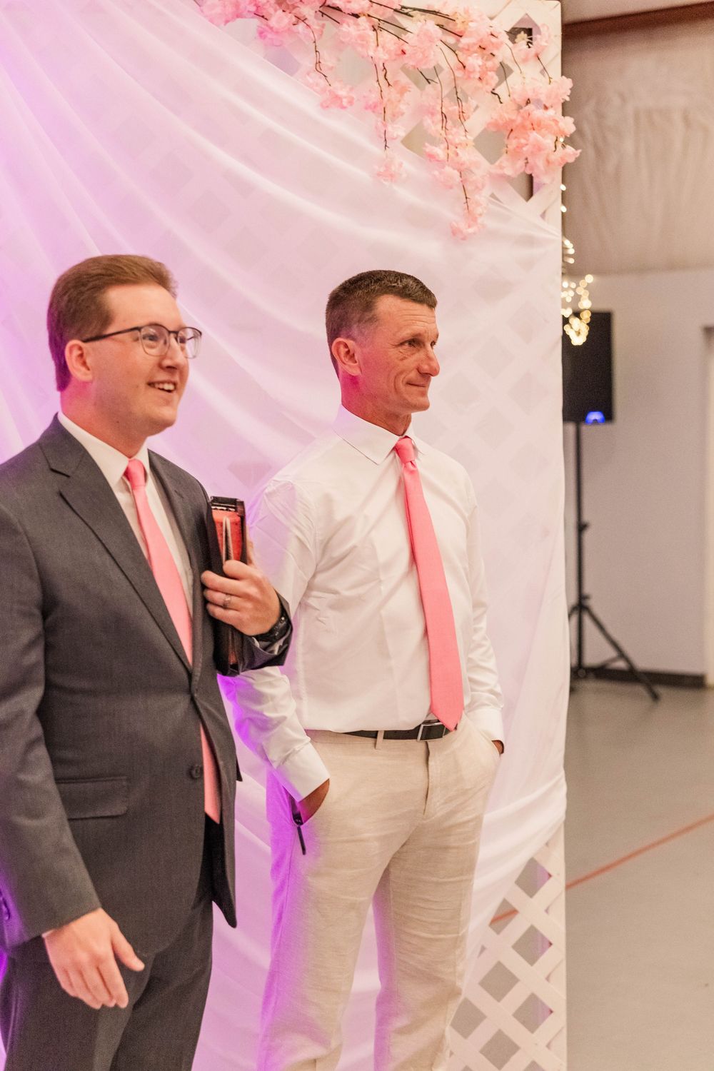 Two wedding party members stand against decorated backdrop with pink cherry blossoms.
