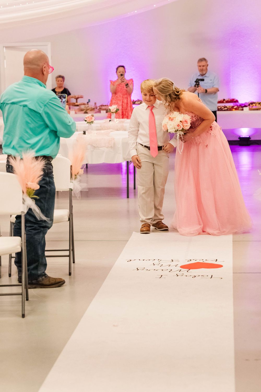 Reception venue decorated in pink and white with formal table settings and ambient lighting.