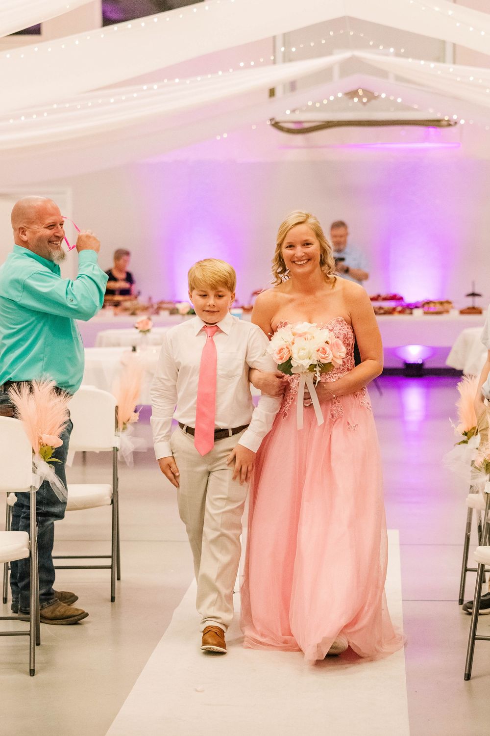 Wedding celebration in a bright venue with pink decor and purple accent lighting.