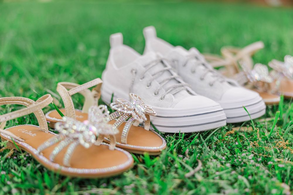 Close-up of bridal footwear with white sneakers and beige sandals on grass.