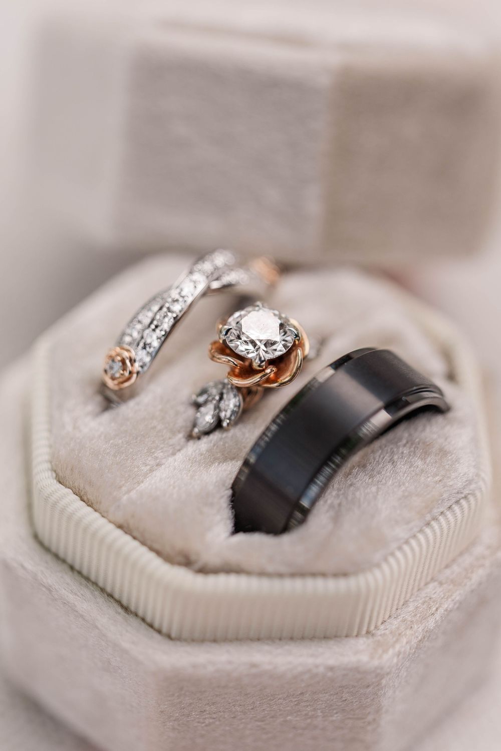 Wedding rings including diamond engagement ring and black band displayed in light gray ring box.