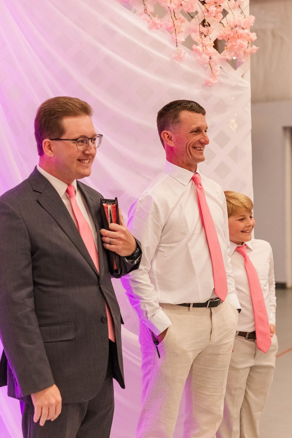 Wedding party members pose together in matching pink ties against decorated backdrop.