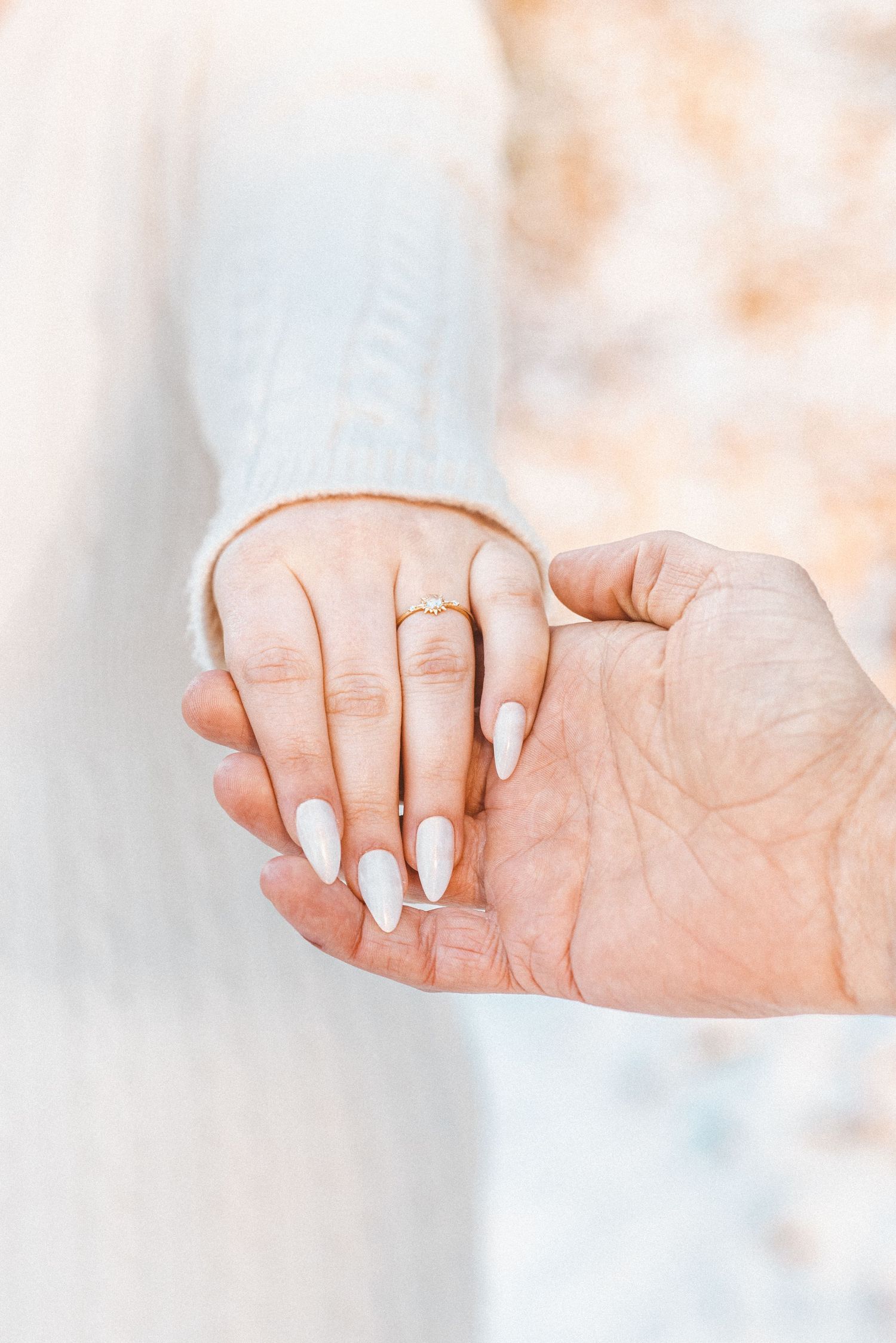 An image of a man holding a woman's hand up to show off a beautiful engagement ring.